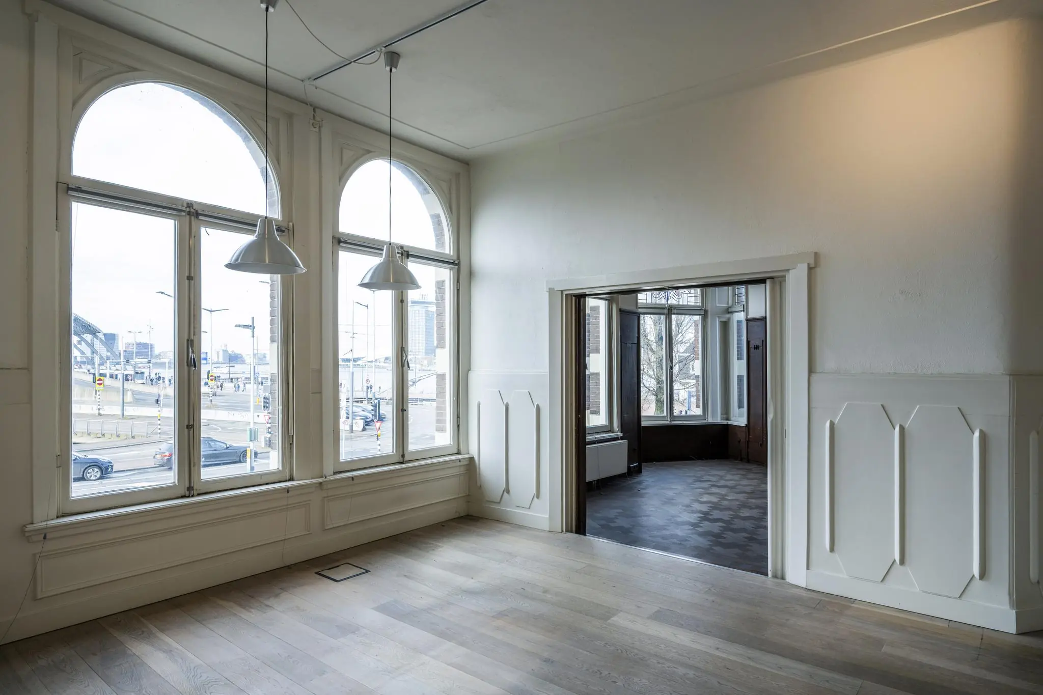 Licht en hoog interieur met grote boogramen aan de De Ruijterkade in Amsterdam, uitkijkend op het stationsgebied.